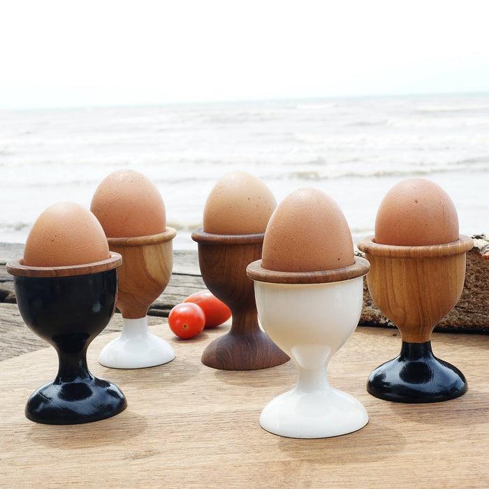 An assortment of different colored teak egg cups with eggs inside placed outside