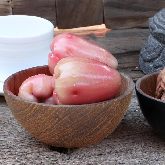 Teak bowl with bell peppers displayed on a wooden surface