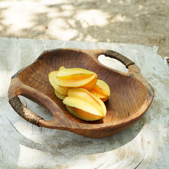 Rico & Plato dora teak serving bowl with rope handles with fruit inside bowl displayed on a wooden surface outside
