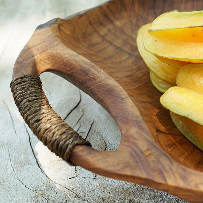 Close up of rope handle of Rico & Plato dora teak serving bowl with rope handles and fruit inside the bowl displayed on a wooden surface