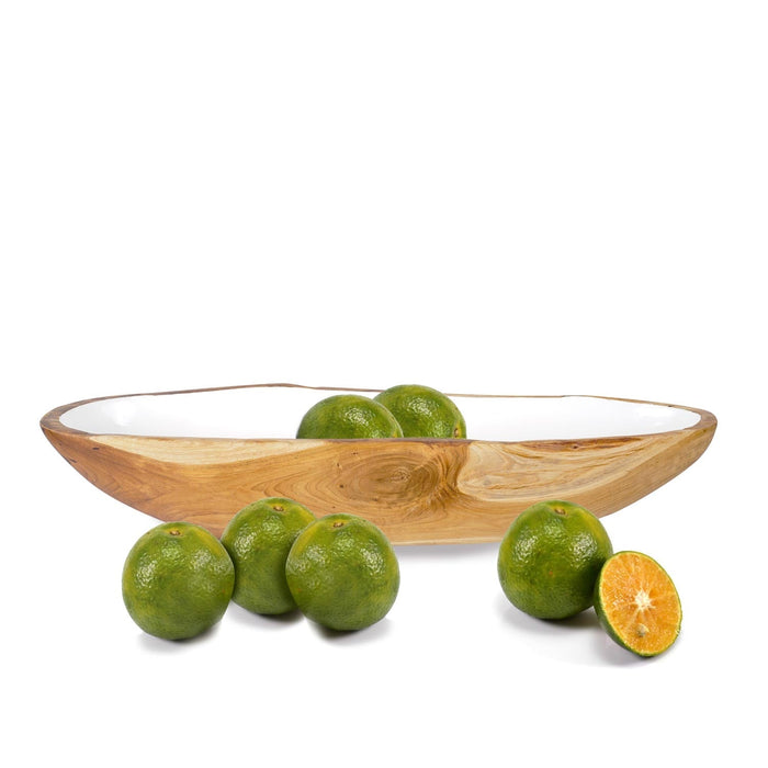 Side view of large teak bowl with white interior filled and next to limes displayed on a white background