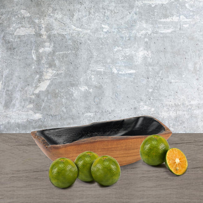 Small teak bowl with black interior with limes on the side displayed on a wooden surface