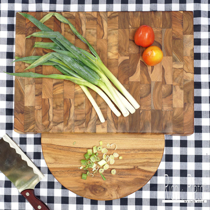 A rectangular teak wood end grain cutting board with a built-in round plate, displayed on a checkered tablecloth with some green onions, tomatoes, and a knife on top.