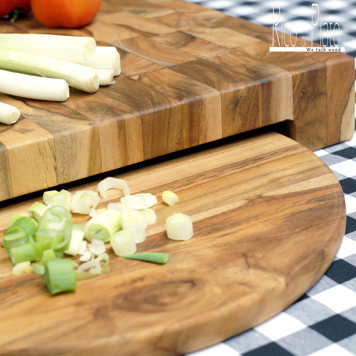 Tomatoes and green onions on a rectangular end grain cutting board with chopped green onions on a round plate placed underneath the rectangular board on a black and white checkered background