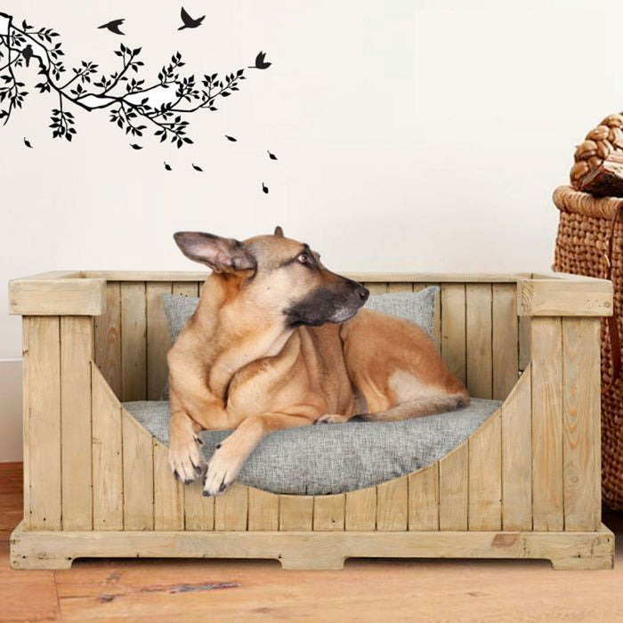 A dog resting on a Rico & Plato large wooden pet bed with cushion placed in a living room setting