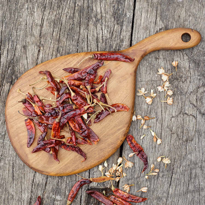 Top view of teak cutting board/serving platter with curved handle and dried chili peppers displayed on a wooden surface