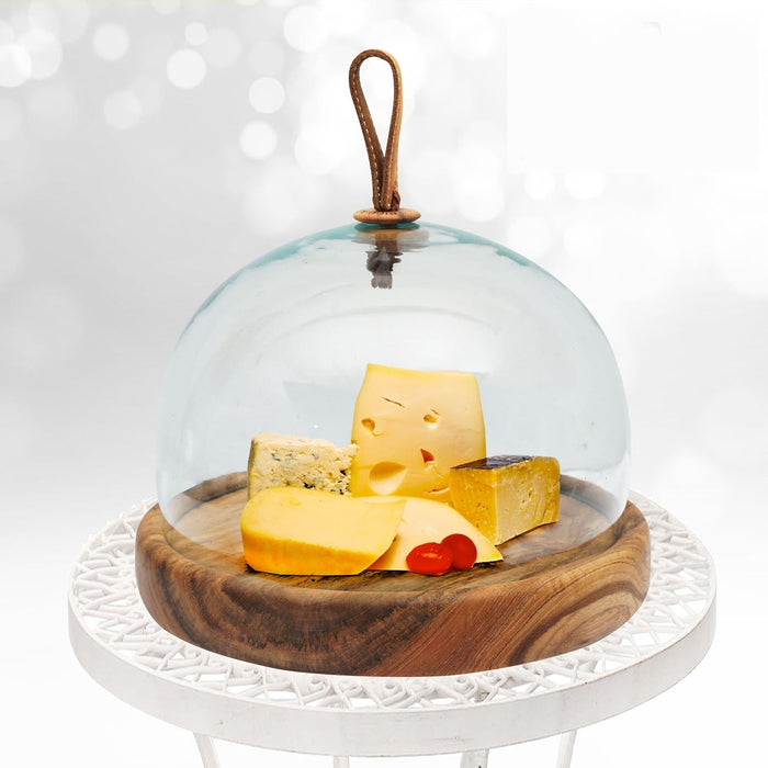 Glass dome cheese platter with cheese blocks inside displayed on a white garden table with a white background