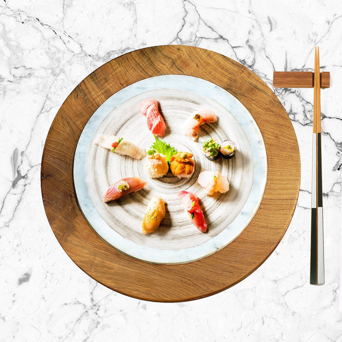 Top view of circular teak sushi server with sushi and chopsticks displayed on a marble surface