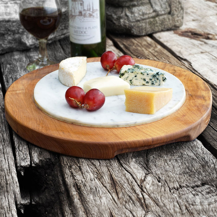 Teak cheese server with integrated handles with cheese and grapes displayed on a wooden surface with wine in the background