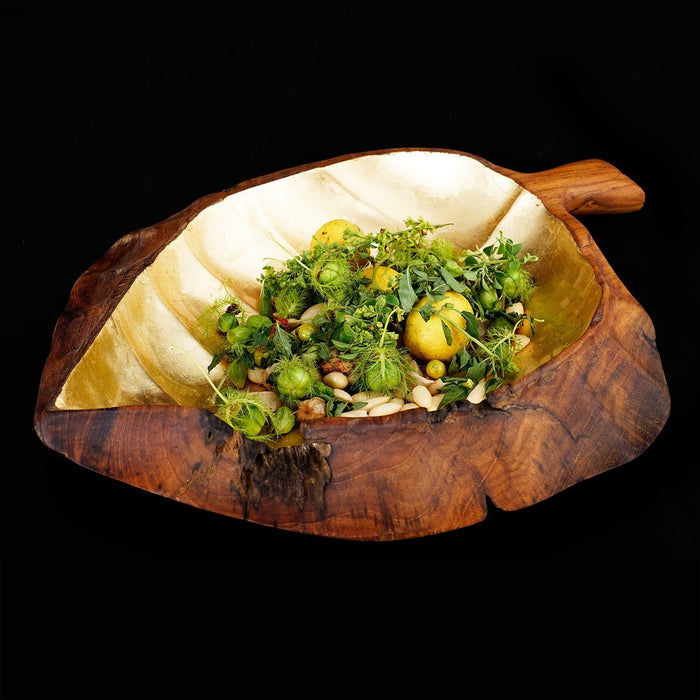 Teak fruit bowl shaped as a leaf with gold leaf interior with an assortment of greens displayed on a black backgrounds