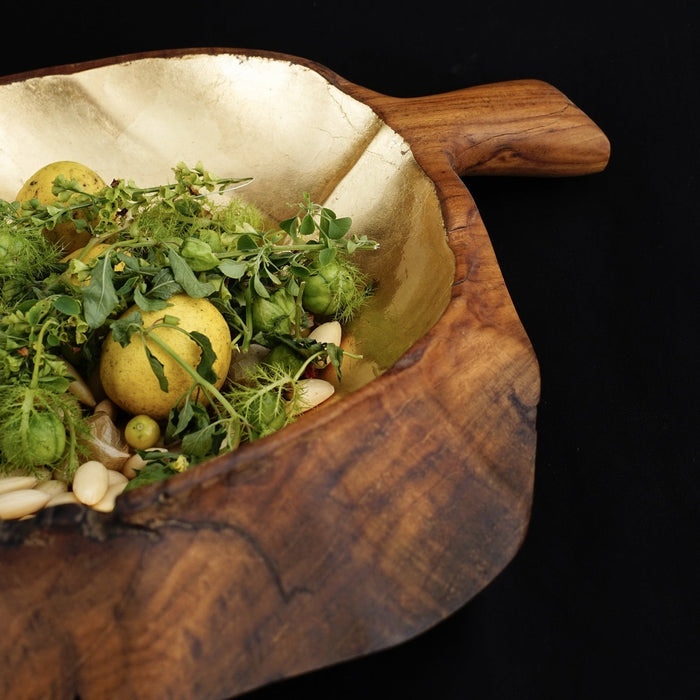 Close up of teak fruit bowl shaped as a leaf with gold leaf interior with an assortment of greens displayed on a black background