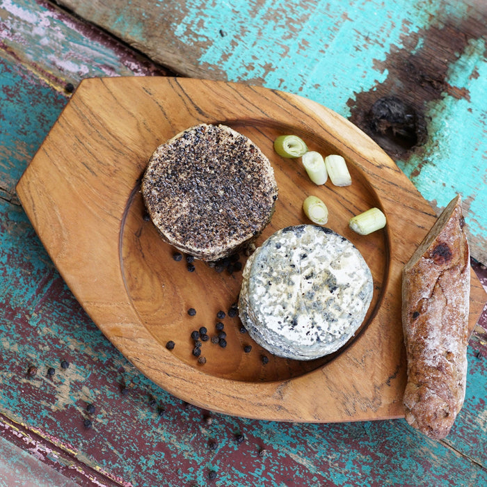 Top view of Rico & Plato granny teak serving platter with cheese, peppercorn, chopped green onions, and a sliced bread displayed on a wooden surface
