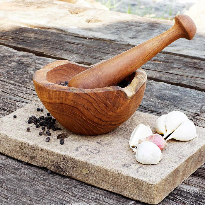 Teak pestle and mortar placed on a block of wood with peppercorn and garlic on a wooden surface