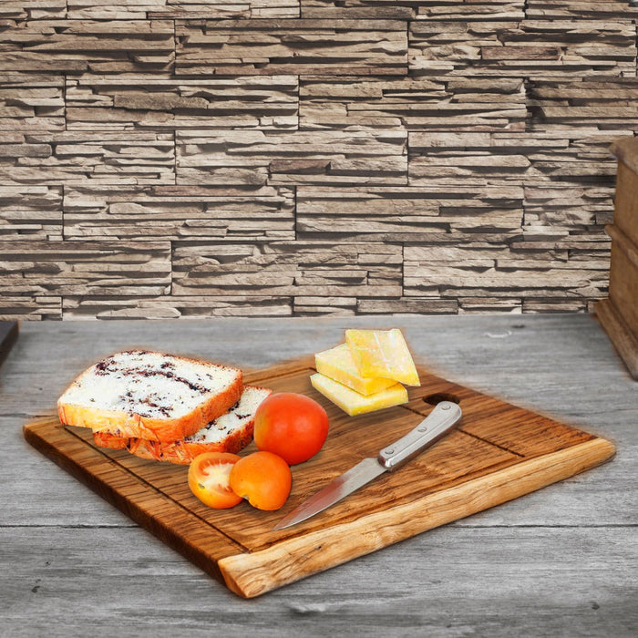 Large teak cutting board with cheese, beard, tomatoes, and knife displayed on a wooden surface