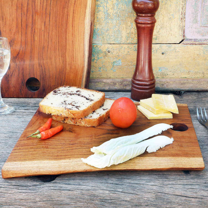 Wooden cutting board with bread, tomatoes, cheese, and lettuce on a rustic wooden surface.