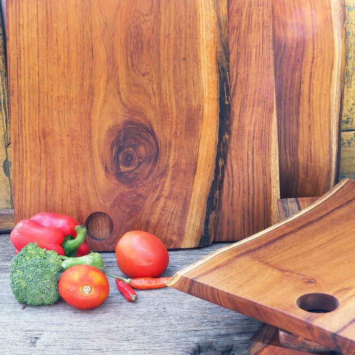 Assortment of small teak cutting board/serving platter next to some vegetables on a wooden surface