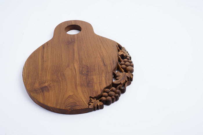 Teak cutting serving board with decoration carved on one side with a handle on the top displayed on a white background