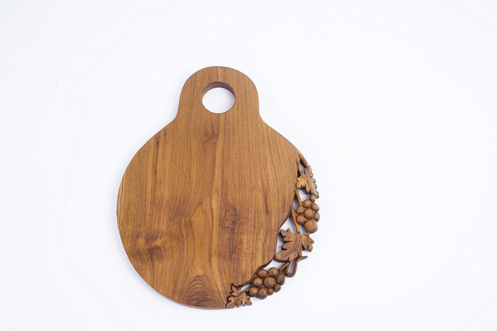 Top view of teak cutting serving board with decoration carved on one side with a handle on the top displayed vertically on a white background