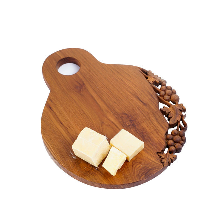 Teak cutting serving board with decoration carved on one side with a handle on the top and blocks of cheese displayed on a white background
