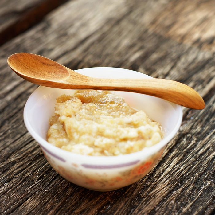 Large wooden baby spoon placed on top of a bowl full of oatmeal on a wooden surface