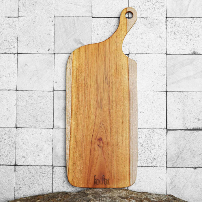 Teak cutting board with natural teak handle and Rico & Plato logo displayed vertically on a tiled background