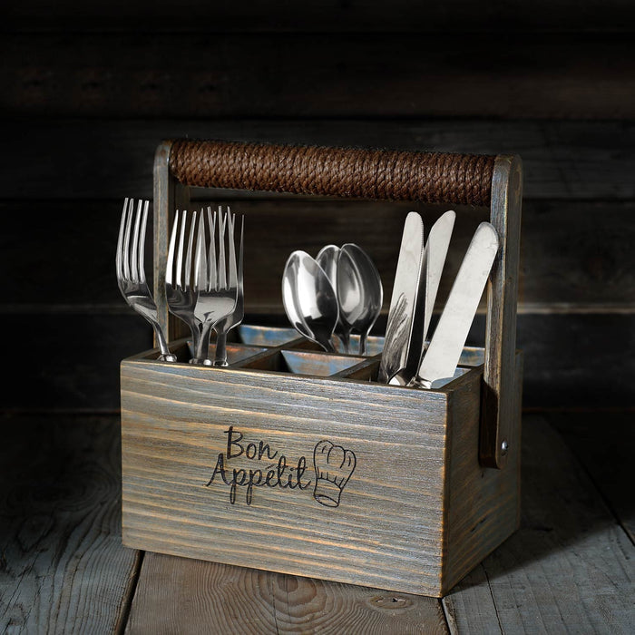 Front view of wooden crate with 'Bon Appetit' engraving and rope handle with silverware placed inside on a wooden surface