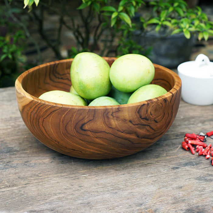Large teak bowl with fruit inside on a wooden surface with a nature background