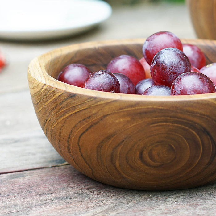 Close up of teak bowl filled with grapes displayed on a wooden surface