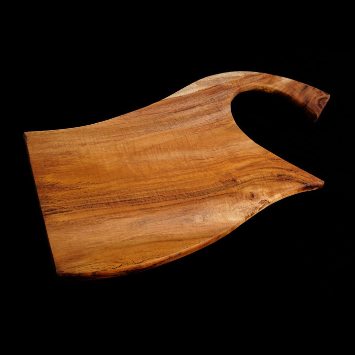 Teak cutting board with curved handle displayed horizontally on a black background
