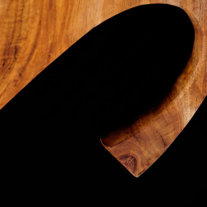 Close up of curved handle of teak cutting board displayed on a black background