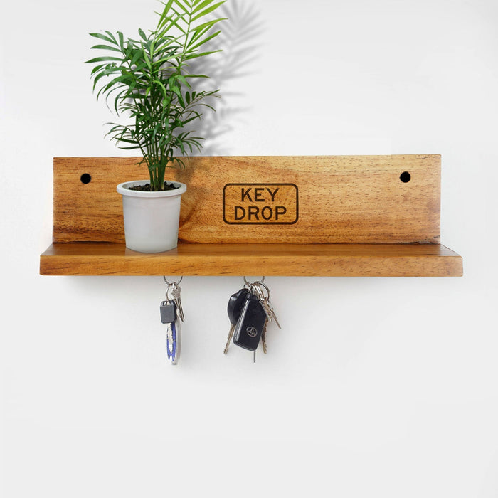 Rico & Plato lucky wooden key hanger displayed on a wall with keys hanging from it and a plant sitting on the ledge of it