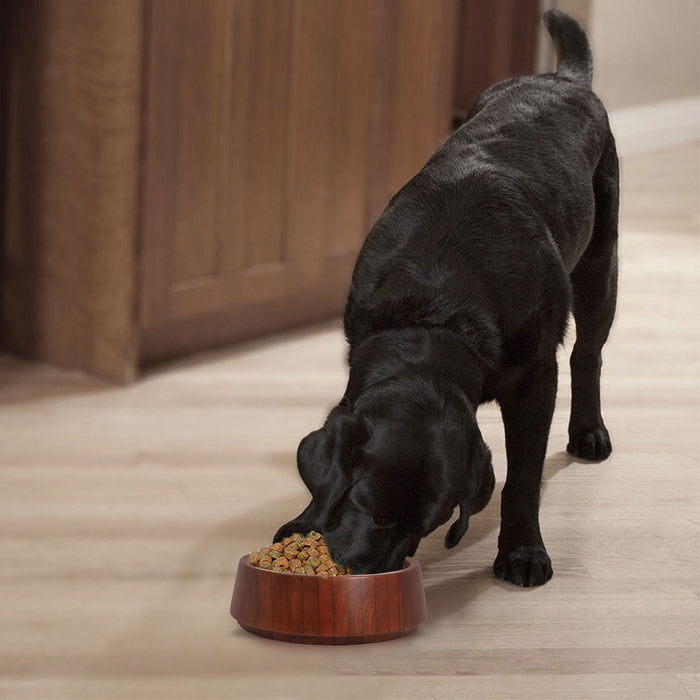 Black dog eating from a mahogany bowl on a wooden floor.