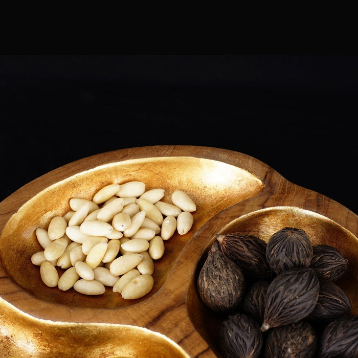 Close up of teak bowl with gold leaf interior with white beans displayed on a black background