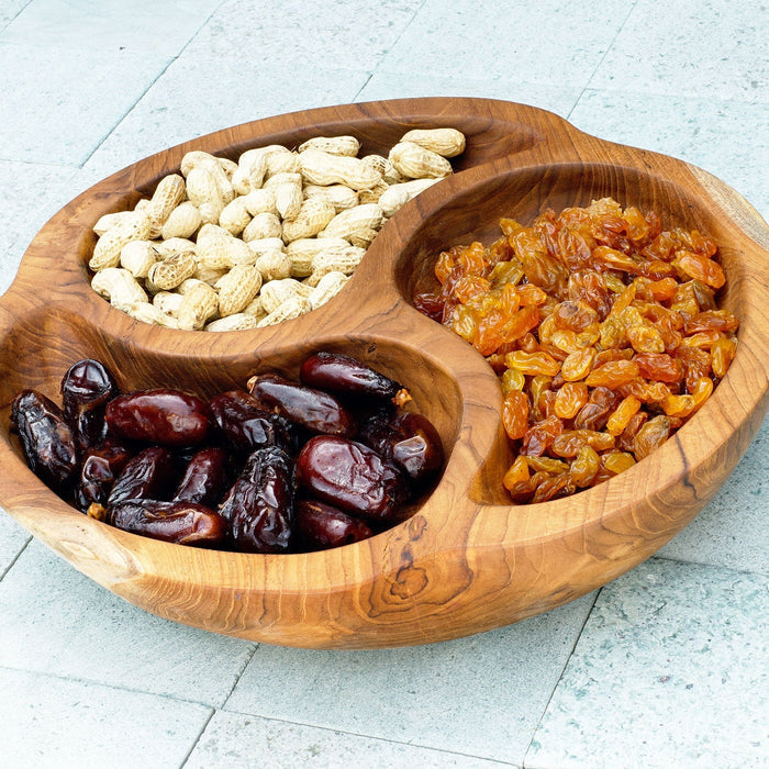 A hand-carved round Manouche Teak wood serving bowl with three compartments containing nuts, dates, and dried fruits.