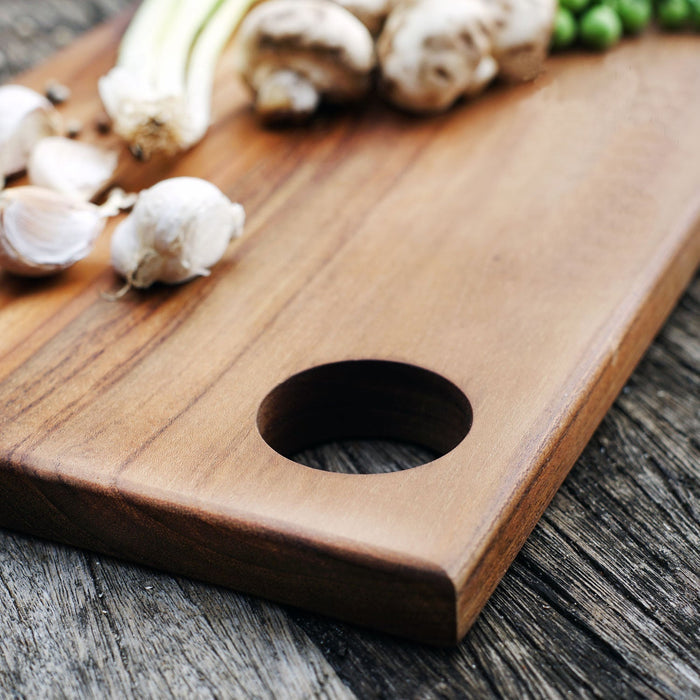 Close up of the hole handle of the rectangle teak cutting board/serving platter displayed on a wooden surface