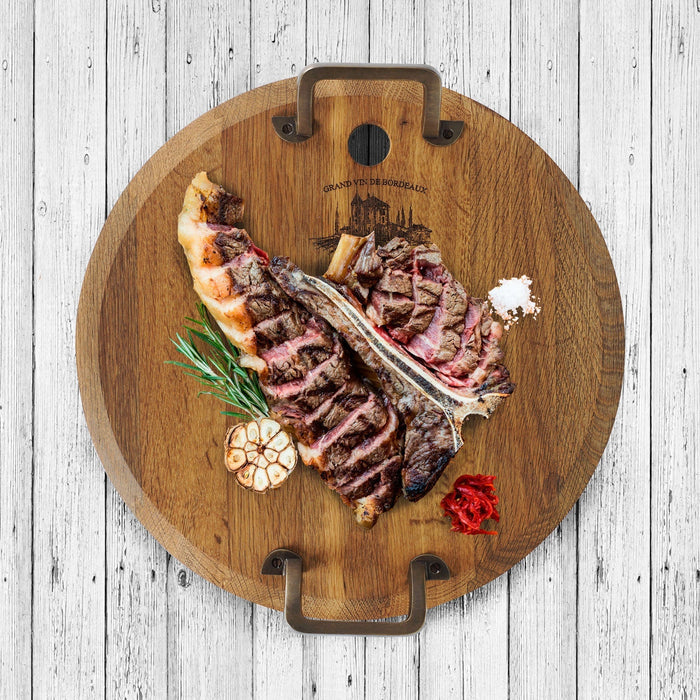 Top view of medium oak serving platter with metal handles and assortment of food on top displayed a white, wooden surface
