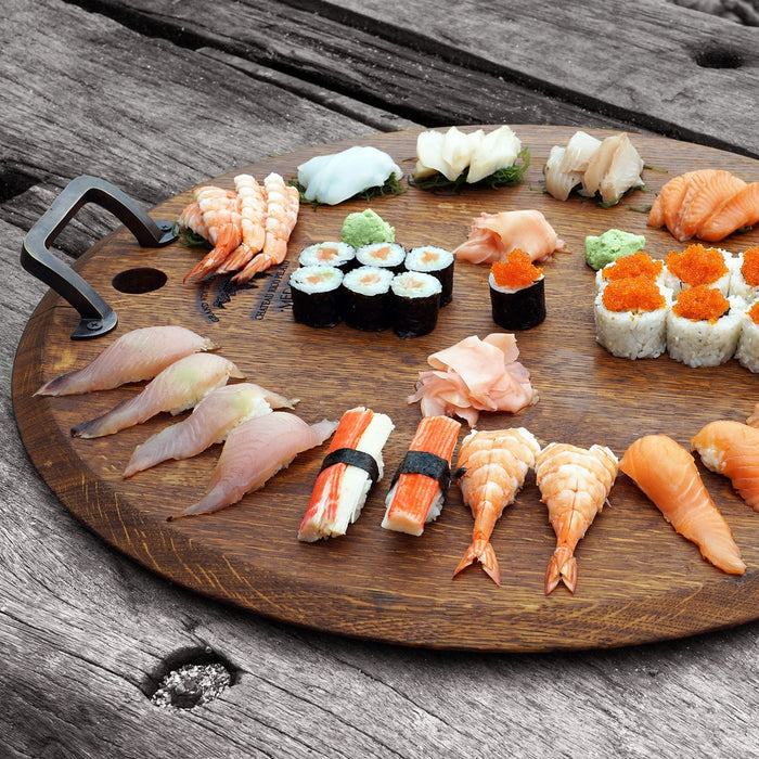 Assortment of sushi displayed on oak serving platter with metal handles displayed on a wooden surface
