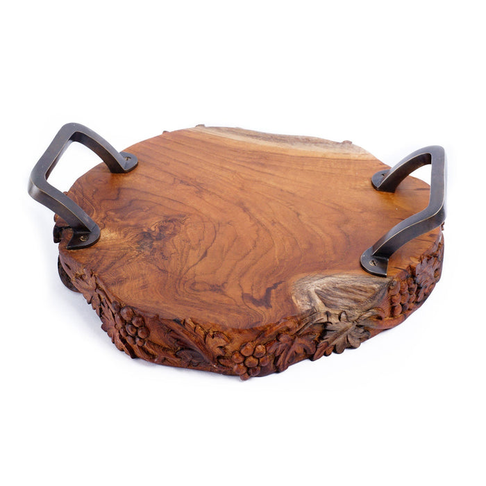 Teak serving platter with metal handles with decorations carved on the side of the serving platter displayed on a white background
