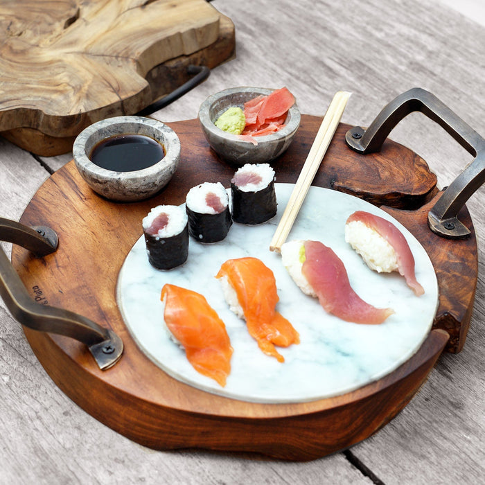 A teak wood sushi server with integrated handles and two gray marble pots, displayed with sushi and dipping sauce on a wooden surface.