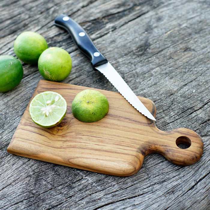 Rico & Plato onilemo teak cutting board serving platter with a cut lime on top next to a knife and 3 limes displayed on  a wooden surface