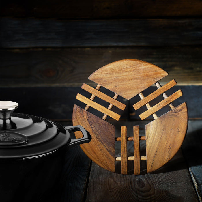 Teak trivet displayed vertically on a wooden surface next to a black stockpot