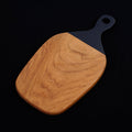Teak cutting board with black handle displayed on a black background