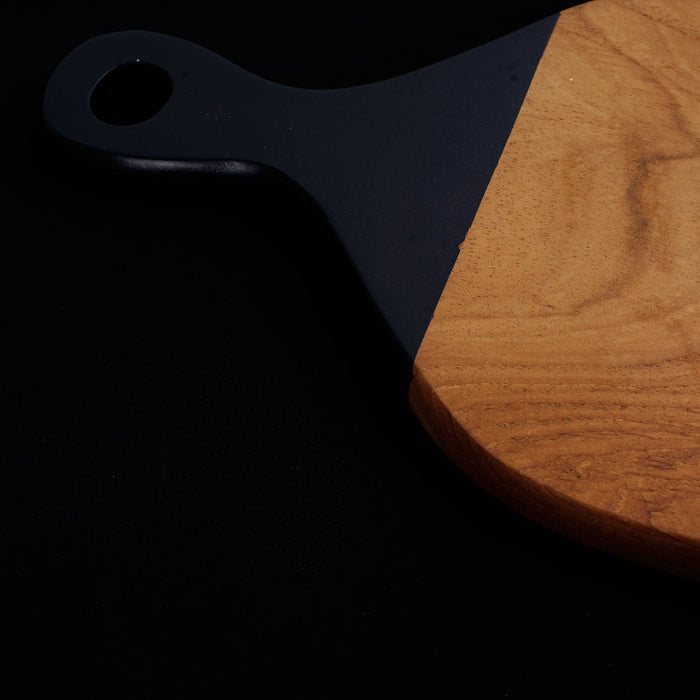 Close up of black handle of teak cutting board displayed on a black background