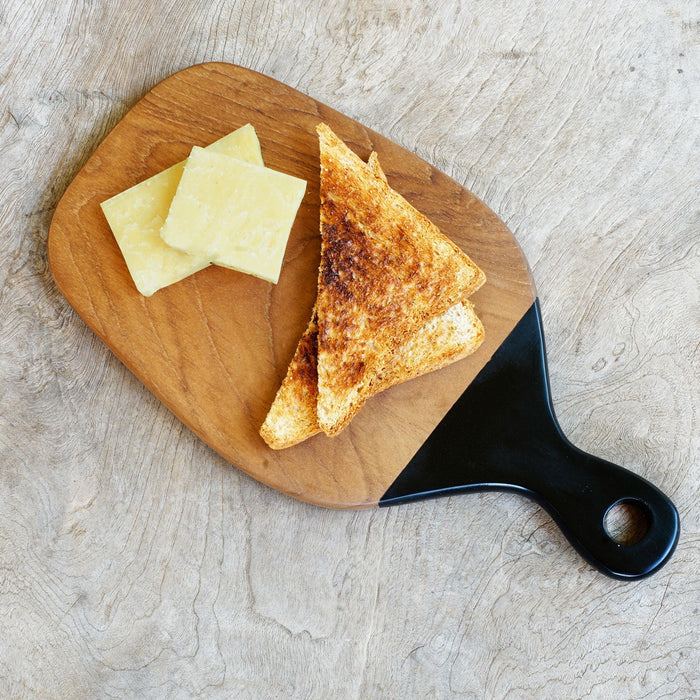 Top view of Teak cutting board with black handle with toast and cheese displayed on a wooden surface