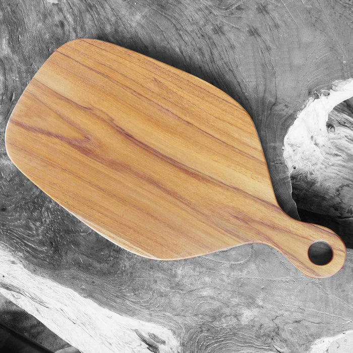Top view of teak cutting board with natural teak handle displayed on a grey marble surface