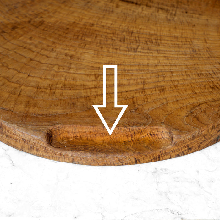 Close up of indent handle with a white arrow pointing at the spot on a teak pizza serving board displayed on a marble counter