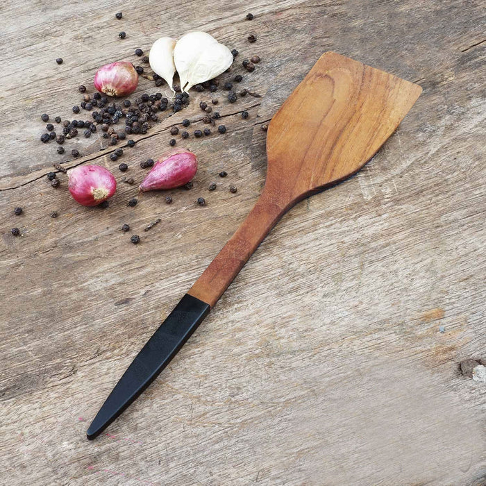 Extra large teak with black handle next to shallot, garlic, and peppercorn displayed on a wooden surface