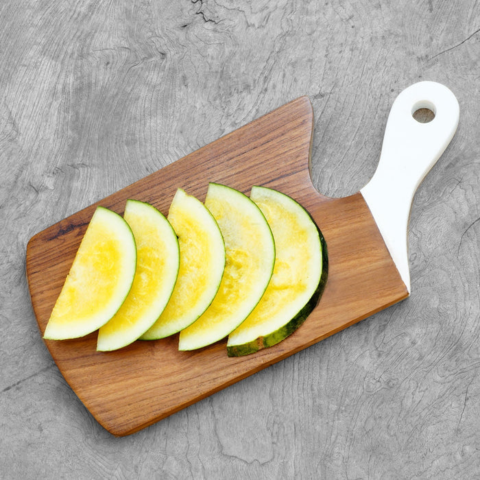 Top view of teak cutting board with white handle with sliced melons displayed on a wooden surface