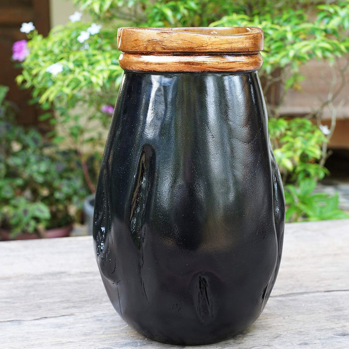 Black teak vase with copper leaf accent rim displayed outside on a wooden surface