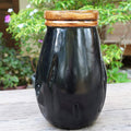 Black teak vase with copper leaf accent rim displayed outside on a wooden surface